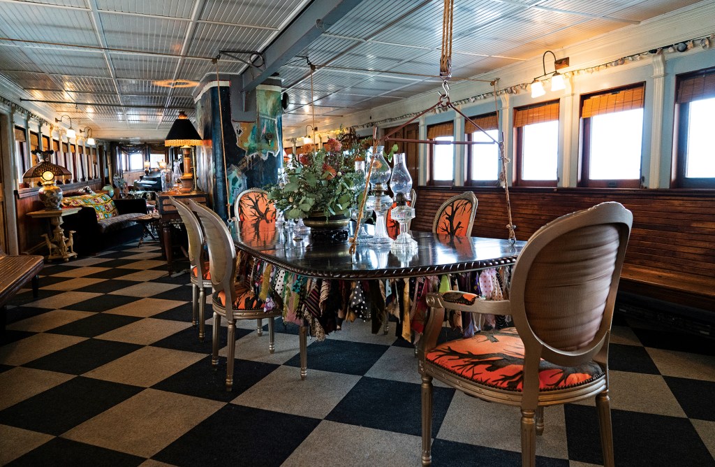 Elegant classic wooden motor yacht interior featuring polished timber paneling, white upholstered built-in seating, a small dining table, and natural light streaming through the vintage portlight windows.