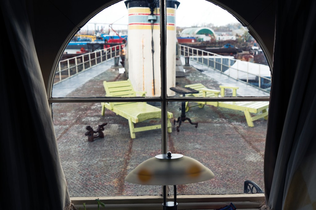A set of weathered metal stairs with rope handrails leading up to the rounded pilothouse of the historic ferryboat Yankee, showing signs of rust on the steps and an industrial harbor background.