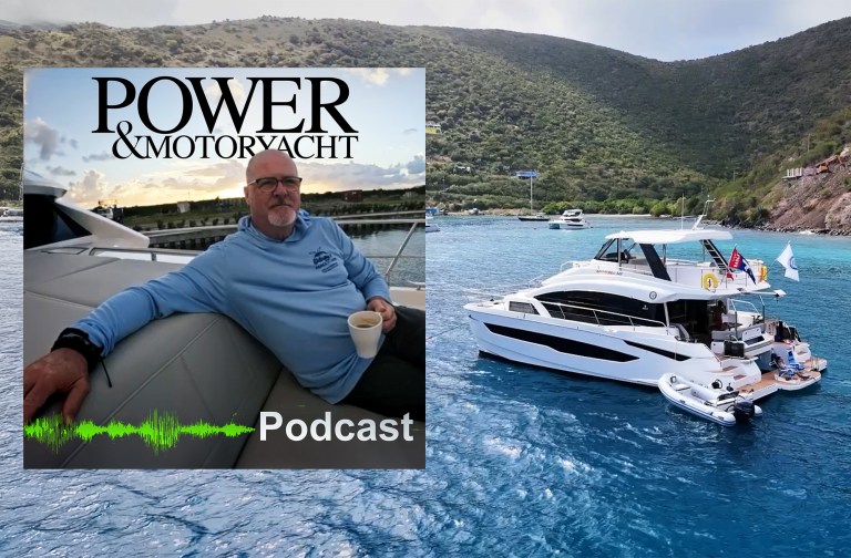 A promotional cover image for the Power & Motoryacht Podcast. The main background shows a sleek, multi-deck white power catamaran anchored in vibrant turquoise Caribbean water near a lush, green, mountainous island coastline under an overcast sky. A small white rigid inflatable boat (RIB) tender is tied up along its broad aft swim platform. Inset on the left is a square portrait of a man with glasses and a goatee wearing a light blue hoodie, relaxing on a yacht's grey exterior cushions while holding a white coffee mug. The top of the inset features the black "POWER & MOTORYACHT" logo, while a green audio soundwave graphic and the white text "Podcast" sit at the bottom.