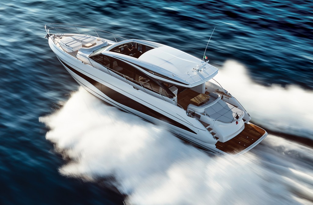 High-angle aerial view of a sleek white Princess V65 motor yacht cruising at high speed, creating large white wakes on deep blue water, highlighting its open sunroof, spacious bow sunpads, and teak aft deck.