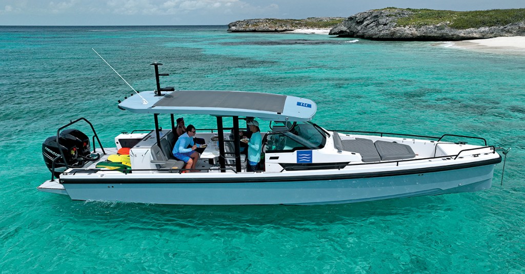 An Axopar 37 Sun Top powerboat carrying several passengers anchored off a tropical island in clear turquoise water.