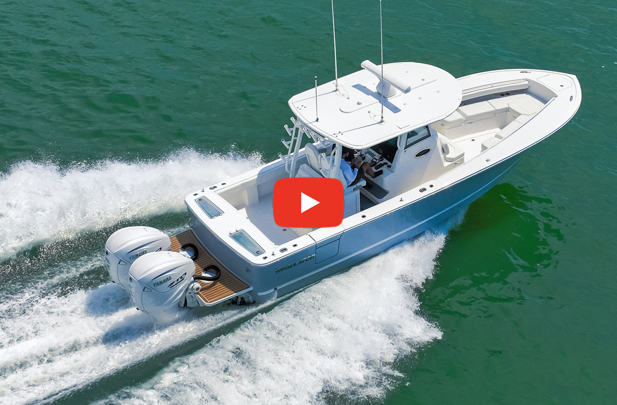 An aerial view of a light blue Regulator 31 center-console powerboat powered by twin white Yamaha outboard engines, running fast through green ocean water with a red video play button overlaid in the center.