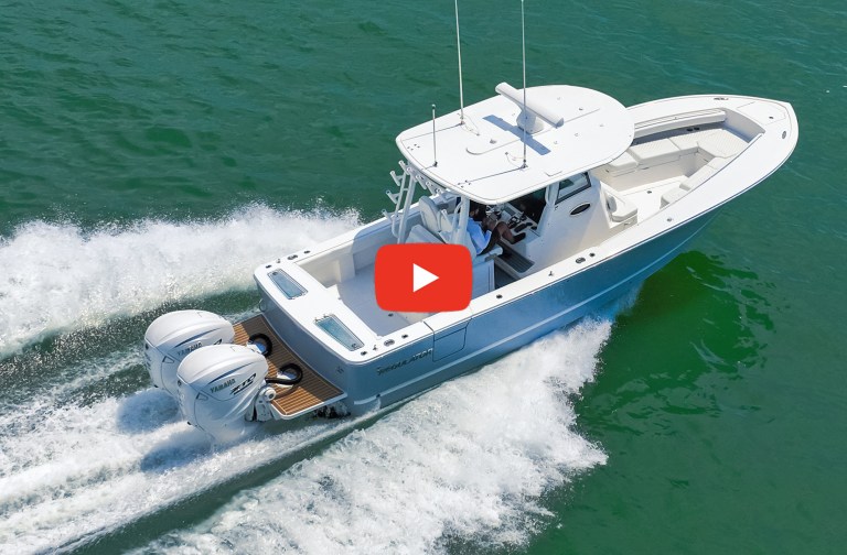 An aerial view of a light blue Regulator 31 center-console powerboat powered by twin white Yamaha outboard engines, running fast through green ocean water with a red video play button overlaid in the center.