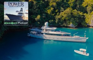An aerial view of the large silver aluminum expedition yacht named "Iceberg" anchored in vibrant turquoise tropical water next to a lush green forested shoreline, with a small white tender boat nearby. A "Power & Motoryacht Podcast" logo is overlaid in the upper-left corner.