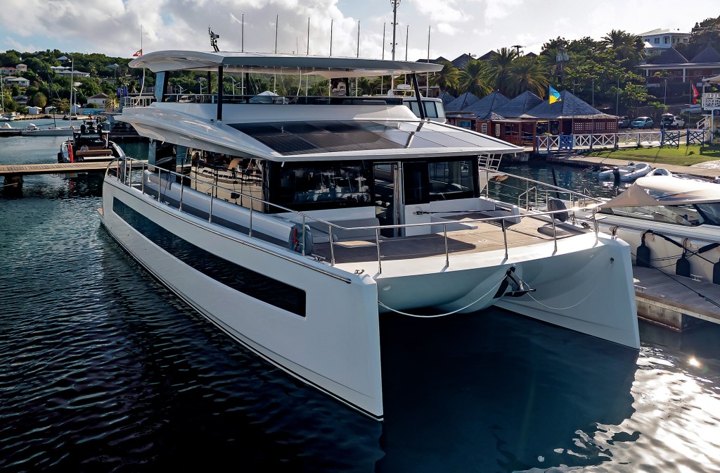 A front-angle shot of a white Silent Yachts solar-electric catamaran docked at a marina, showcasing its wide multihull bow and solar panel array stretching across the upper decks.