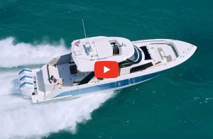 An aerial view of a white and blue luxury powerboat equipped with triple outboard engines cruising across clear ocean water, with a YouTube play button overlay in the center.