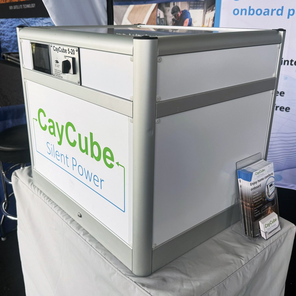 A standalone white and aluminum CayCube Silent Power generator unit sitting on a display table next to promotional brochures at an event exhibit.