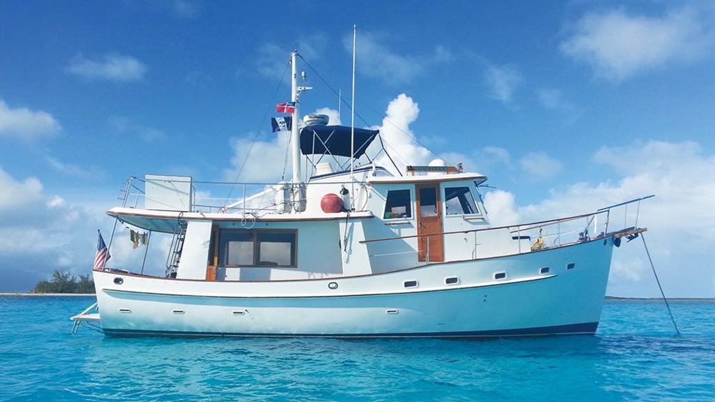 A side profile photograph of a classic Kadey-Krogen 42 trawler named Dauntless anchored in vibrant turquoise tropical waters under a bright blue sky.