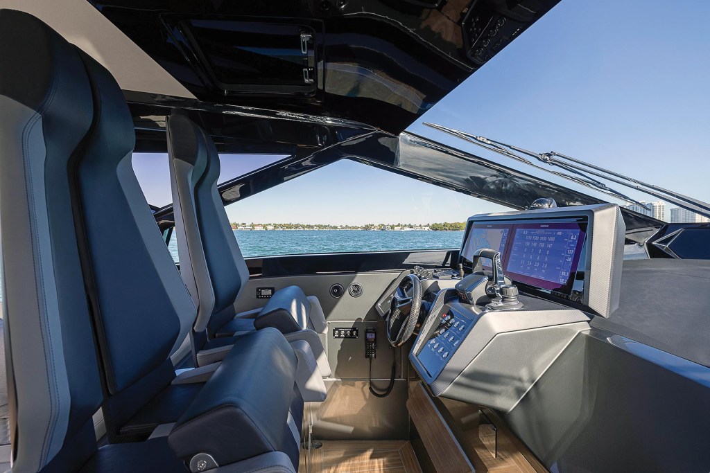 The futuristic helm station of a Wallypower 50X, featuring high-backed sport seats, dual electronic multifunction displays, angular glass windshield frames, and a sports steering wheel looking out onto open water.