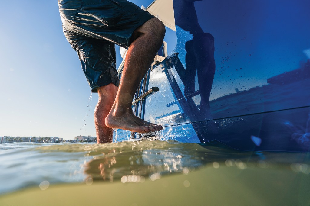 A swimmer climbing a stainless-steel boarding ladder attached to the blue hull-side door of an Intrepid 35 Valor boat.