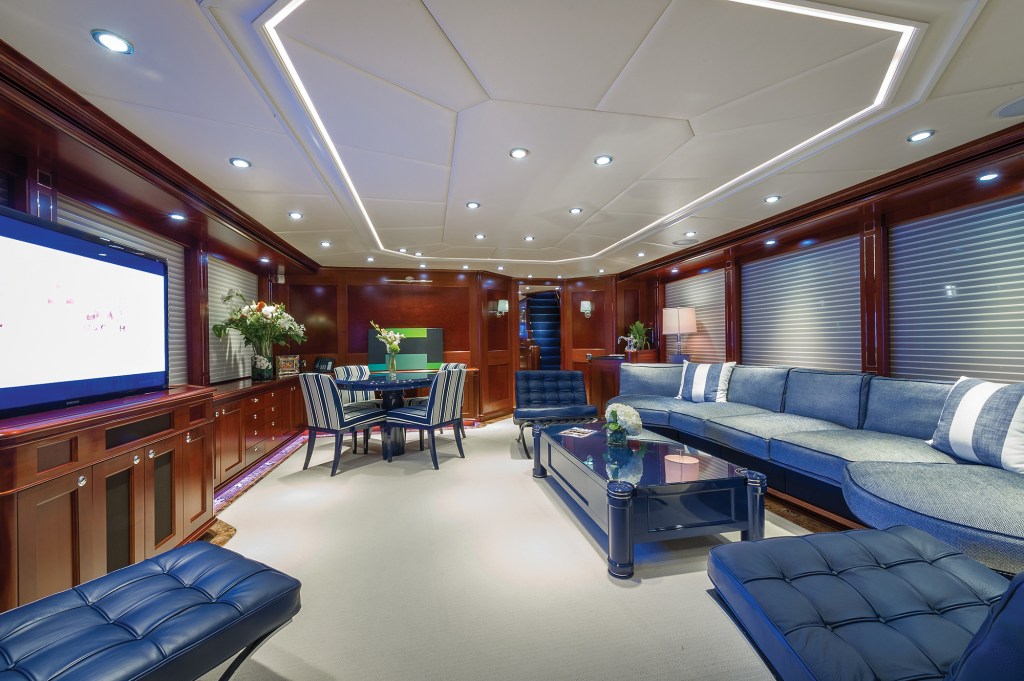 Luxurious main salon interior of the yacht Beothuk featuring plush blue seating, polished wood cabinetry, recessed ceiling lighting, and a dining table.