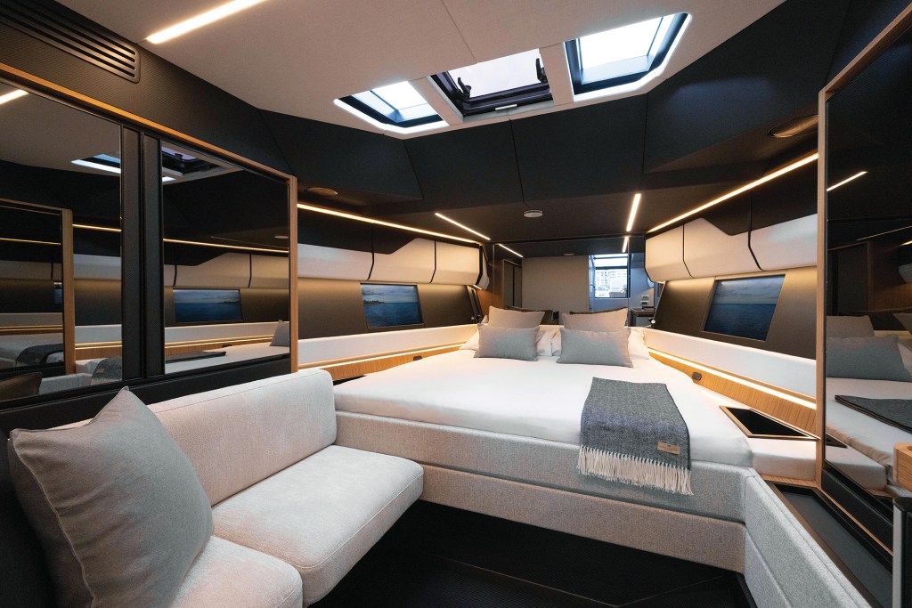 The modern lower cabin of a Wallypower 50X featuring a forward island berth, mirrored accent panels, overhead skylights, and digital camera screens along the hullsides projecting real-time ocean views.