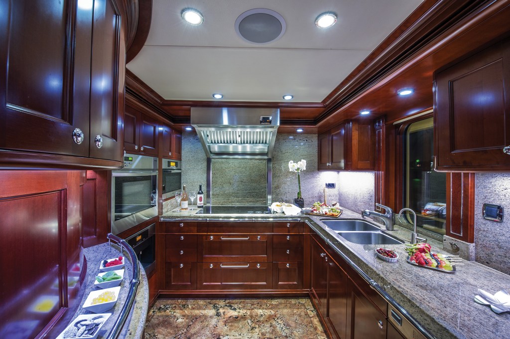 The fully equipped galley aboard the yacht Beothuk, featuring rich cherry wood cabinetry, granite countertops, double sinks, and stainless-steel appliances.