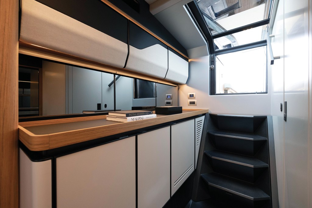 The lower deck entryway of a Wallypower 50X featuring modern cabinetry with wood trim, integrated storage, ambient lighting, and dark geometric steps leading up toward the main deck.