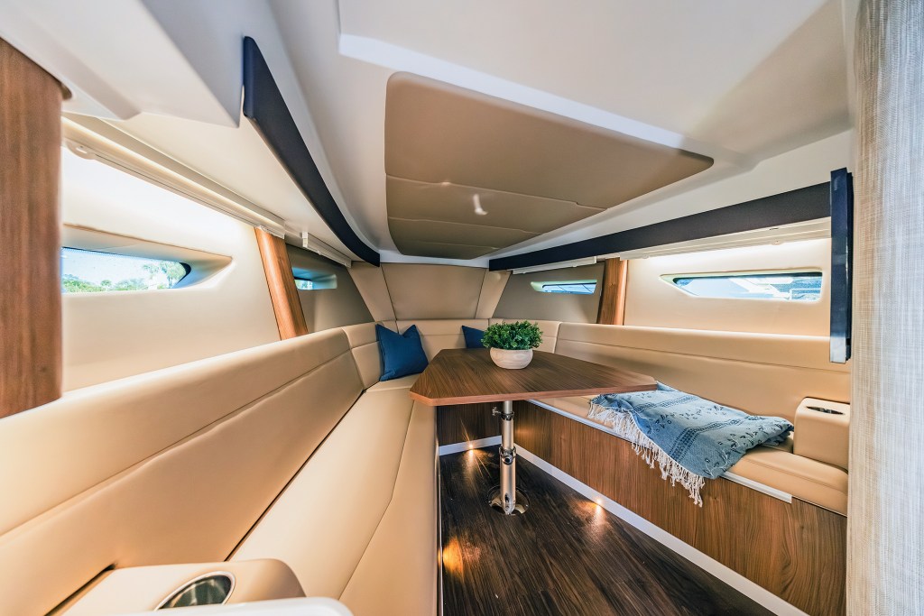 The forward cabin lounge aboard an Intrepid 35 Valor featuring a convertible V-berth dinette table, cream leather seating, and wood accents.