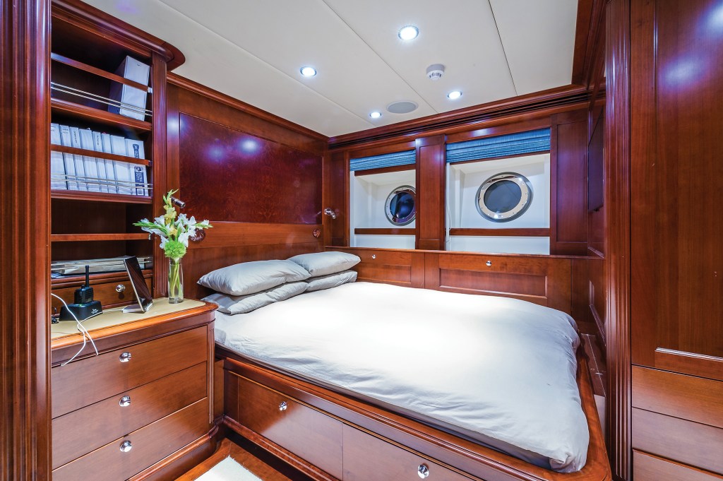 A stateroom aboard the yacht Beothuk featuring a built-in double bed, polished mahogany woodwork, nightstand storage, and twin round portholes.
