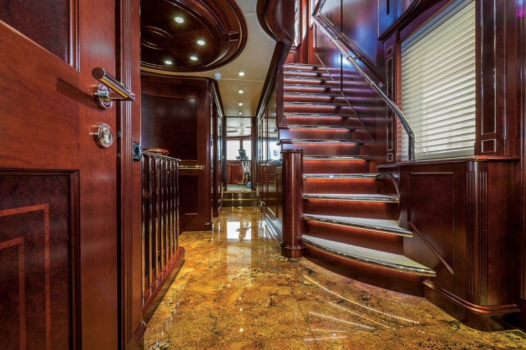 Interior hallway of the yacht Beothuk showcasing polished marble flooring, rich wood panelling, and an illuminated staircase leading to the upper deck.