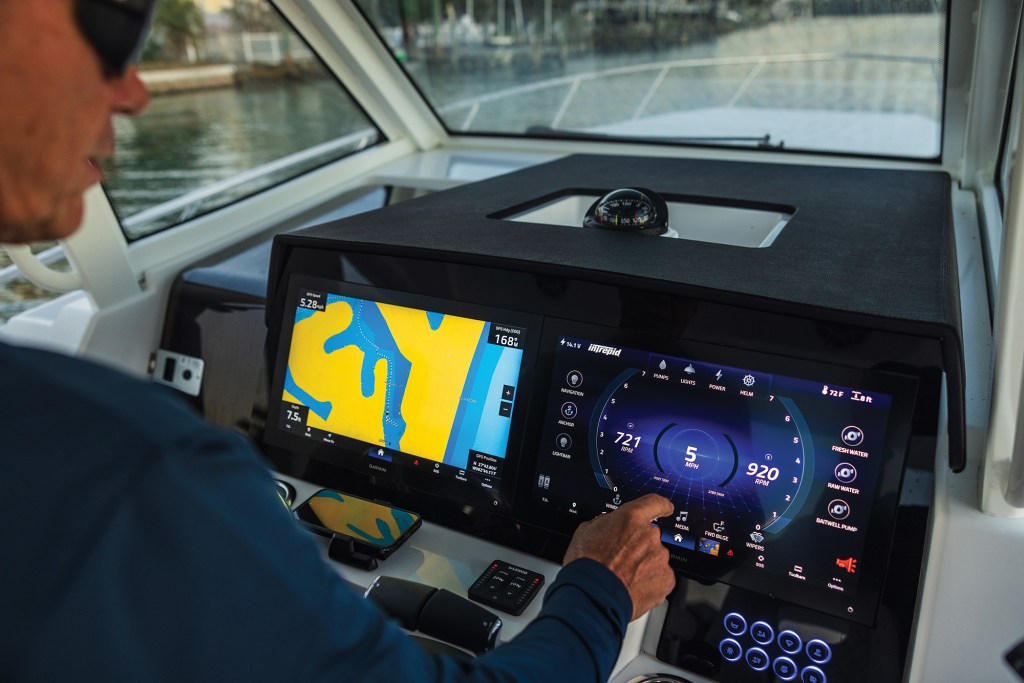 A captain operating the digital helm console on an Intrepid 35 Valor, featuring dual flush-mounted Garmin touchscreen displays showing navigation charts and engine performance data.