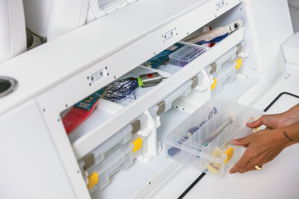 Built-in tackle storage cabinet integrated into the mezzanine seating workstation of an Intrepid 35 Valor boat, with a hand pulling out a clear plastic lure box.