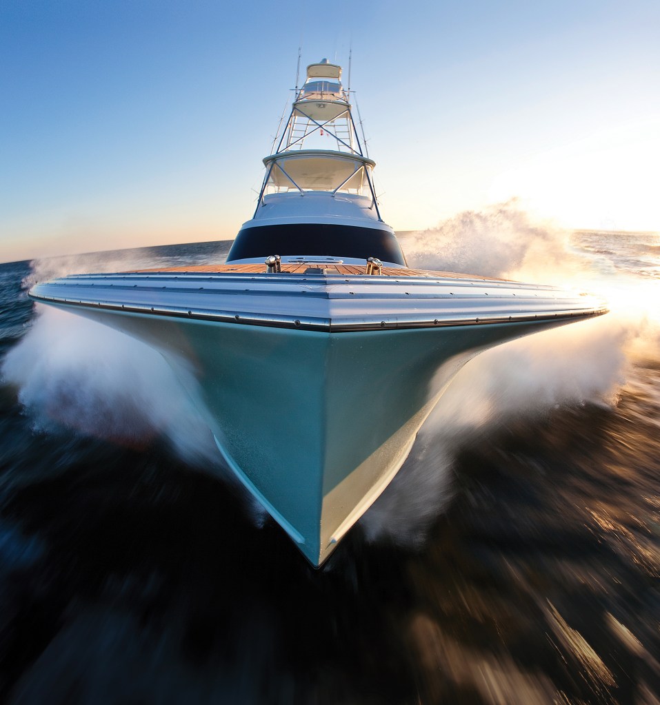 A dramatic low-angle bow shot of a Jarrett Bay custom sportfish yacht running at high speed, showcasing its extreme Carolina bow flare as it cuts through the water.