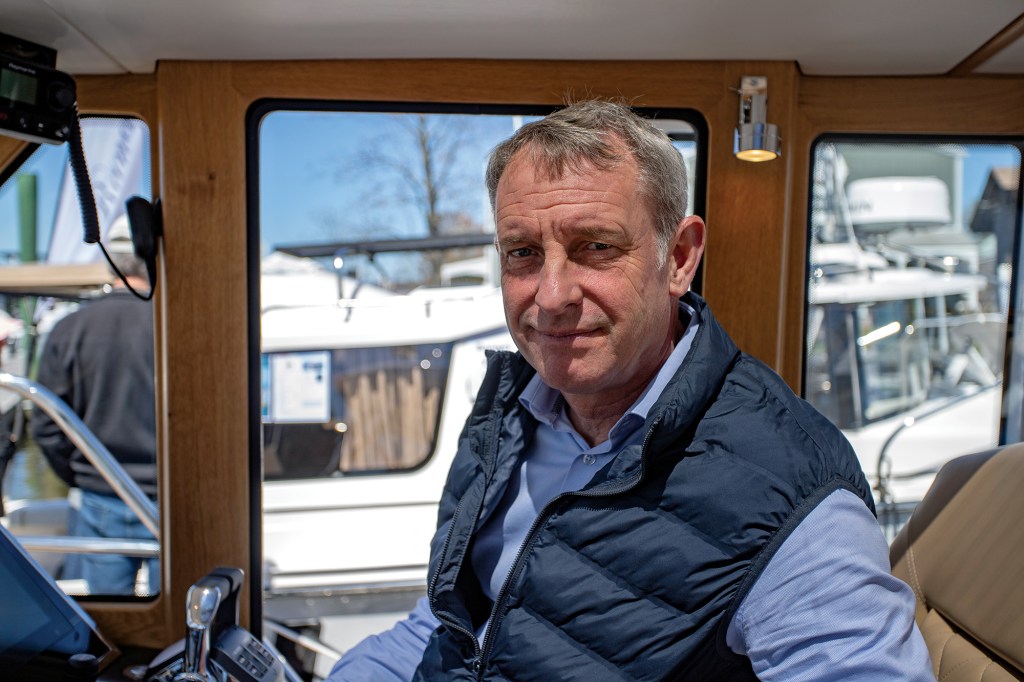 A portrait of Cockwells founder Dave Cockwell sitting at the helm inside the wooden-trimmed wheelhouse of a motor yacht.