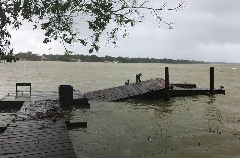 feat_Ode to a Loyal Dock A damaged wooden floating dock collapsed into rough, wind-rippled coastal waters under an overcast sky following a severe storm.