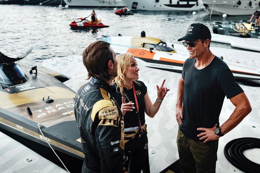 Tom Brady speaking with Team Brady RaceBird pilots Sam Coleman and Emma Kimiläinen in front of their electric raceboat.