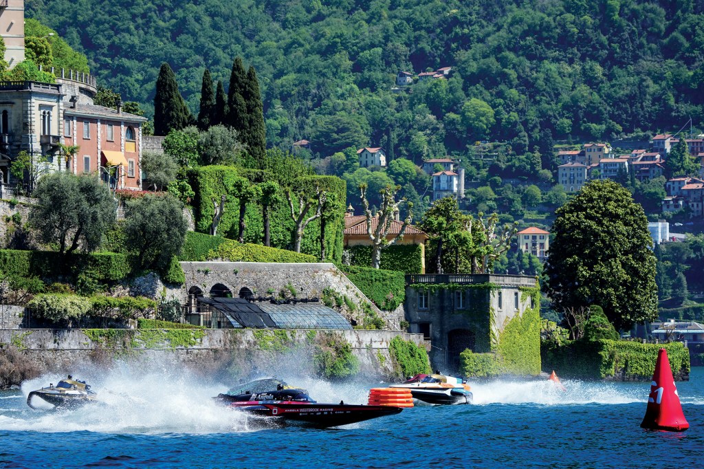 Electric RaceBird boats speeding around a red turn buoy past historic villas on Lake Como during an E1 powerboat race.