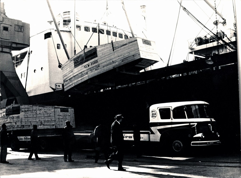 Vintage black-and-white photograph of a wooden crate containing a Riva speedboat labeled NEW YORK being loaded onto a cargo ship.