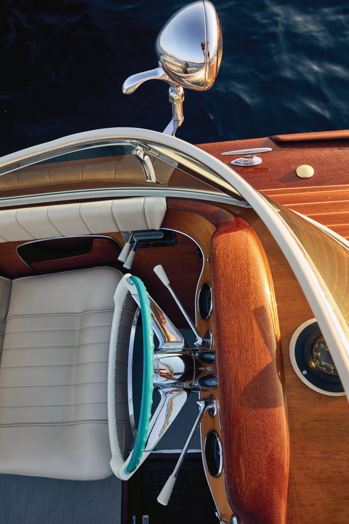 Classic helm station of a vintage wooden Riva Aquarama featuring a turquoise and white steering wheel, chrome spotlight, and polished mahogany dashboard.