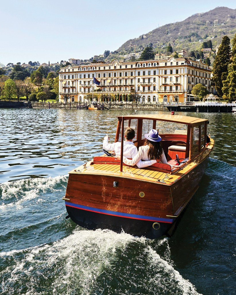 Couple riding in a classic wooden Vaporina motorboat towards the luxury hotel Villa d'Este on Lake Como.