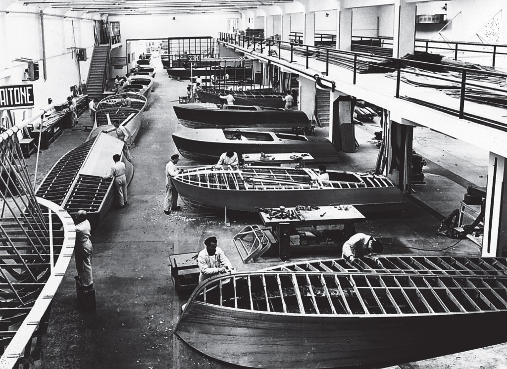 Vintage black-and-white photograph of craftsmen constructing wooden speedboats inside the historic Riva shipyard factory floor.
