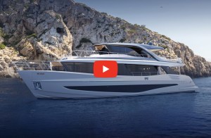 A white luxury motor yacht, the Princess X90, navigating calm blue water with a steep, rocky cliffside in the background under a clear sky. A red play button icon is overlaid in the center of the yacht.