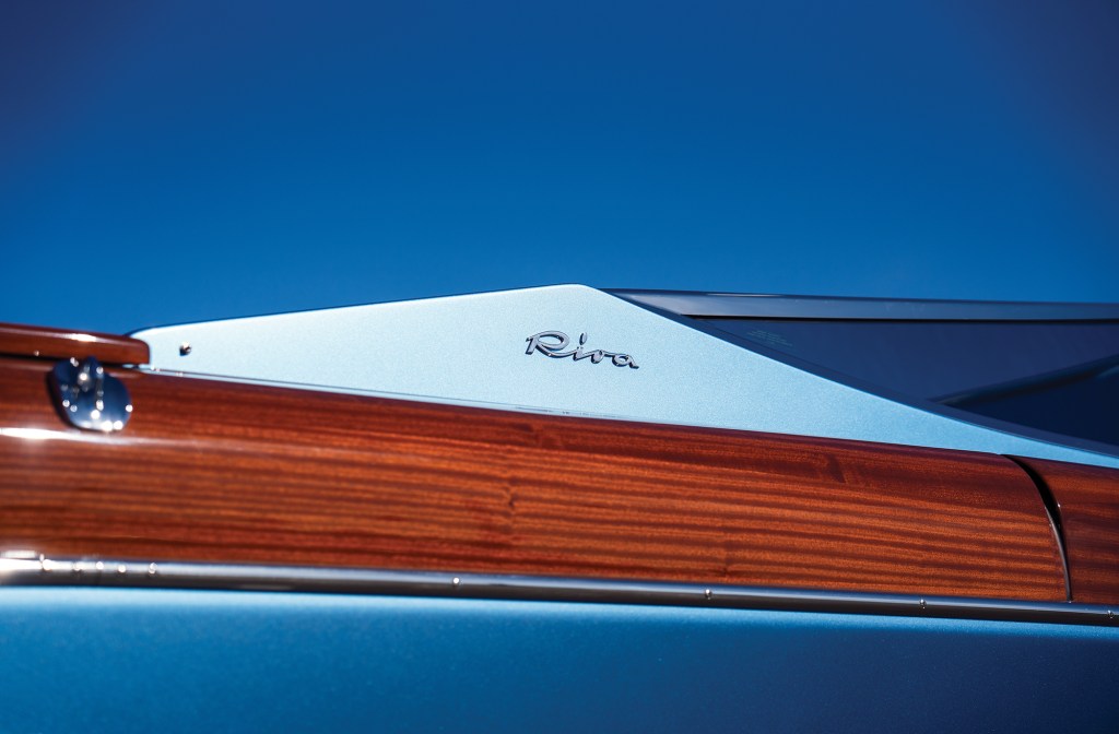 Close-up view of polished mahogany wood trim and the chrome Riva emblem on a luxury speedboat deck.