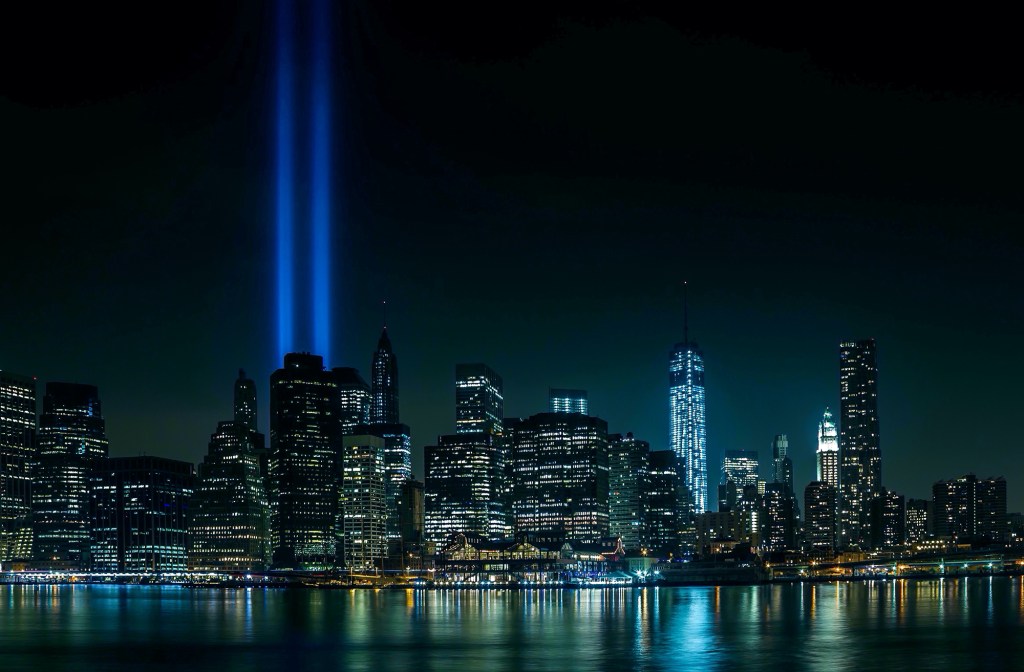 9/11 The New York City skyline illuminated at night featuring the Tribute in Light search beams shining into the sky near One World Trade Center.