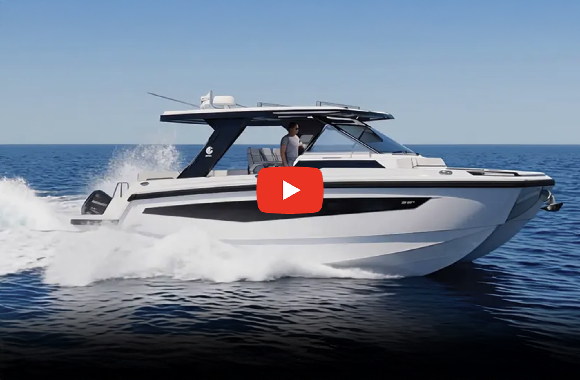 A modern white and black power catamaran cruising rapidly across blue open water, splashing wake behind it, with a person standing at the helm under a hardtop roof and a prominent red video play button overlaid in the center.