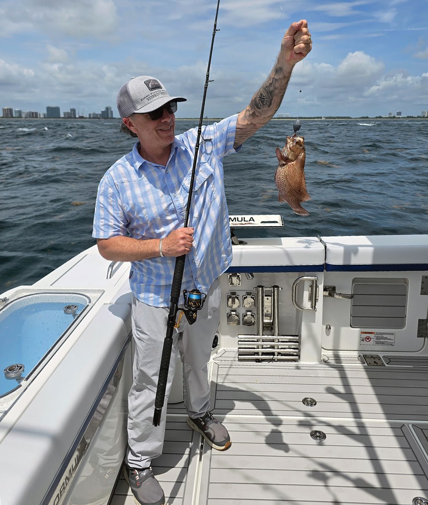 A angler smiling while holding up a caught fish on the stern deck of a Formula center console boat.
