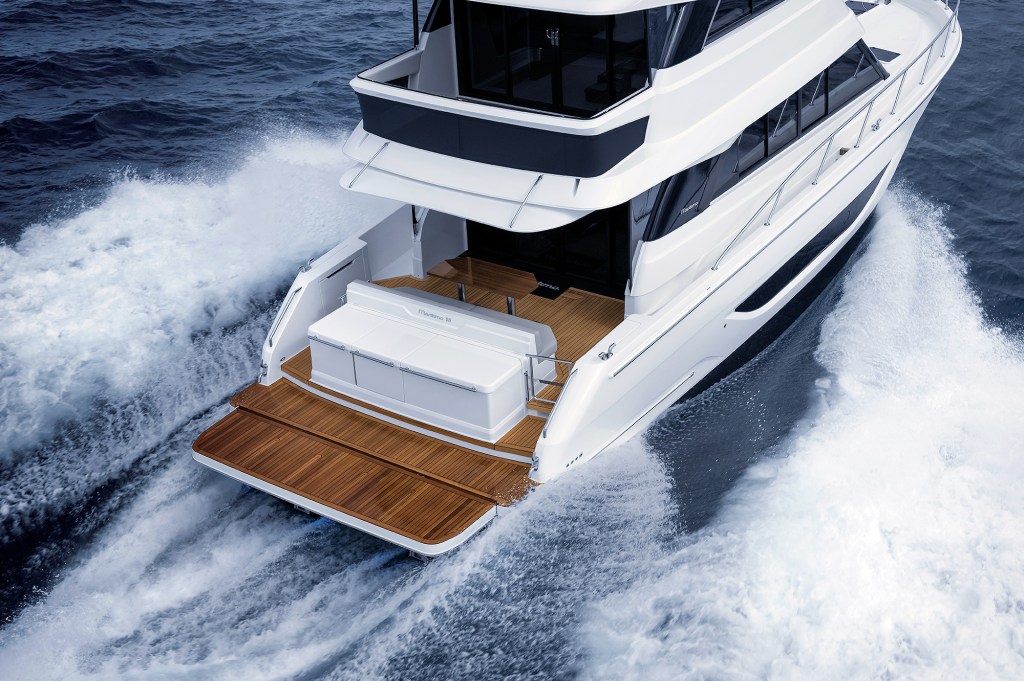 High-angle view looking down at the aft deck, teak swim platform, and seating area of a Maritimo M50 yacht cruising at speed through choppy water.