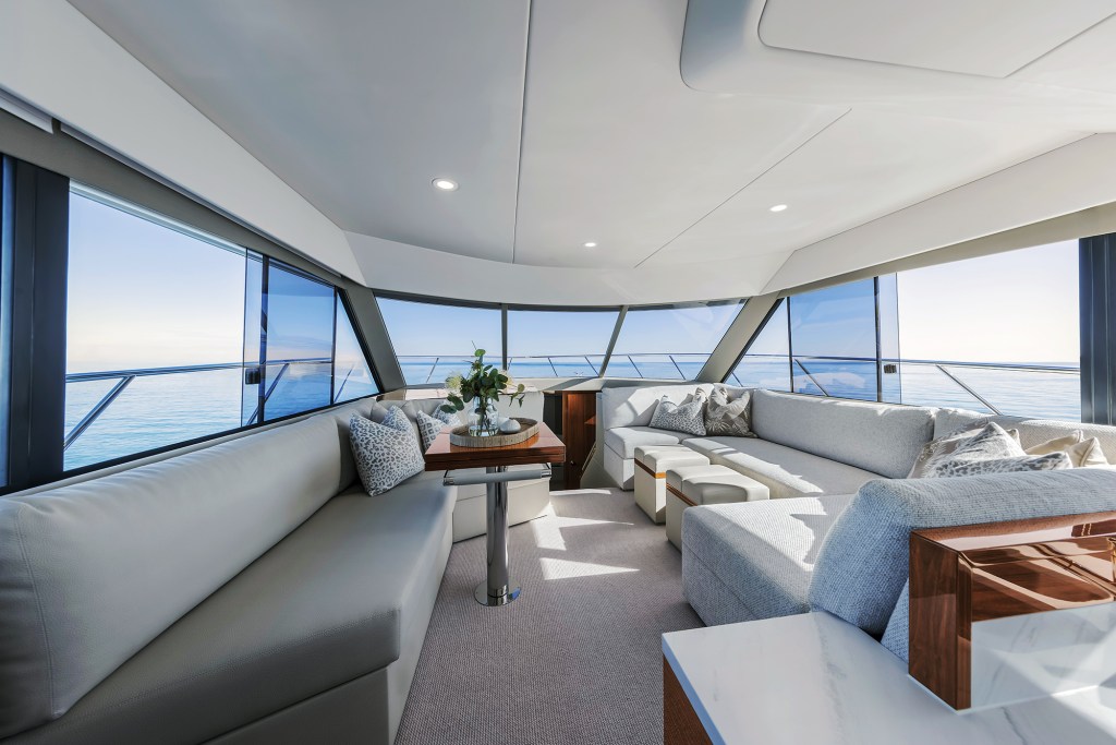 The bright, open main salon of a Maritimo M50 yacht featuring large side windows, L-shaped upholstered settees, and a central dining table with ocean views.