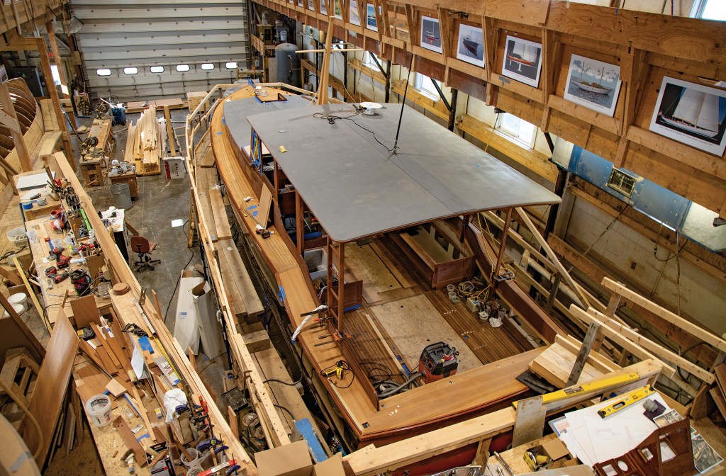 High-angle view of a custom wooden boat under construction inside the traditional workshop of Brooklin Boat Yard.