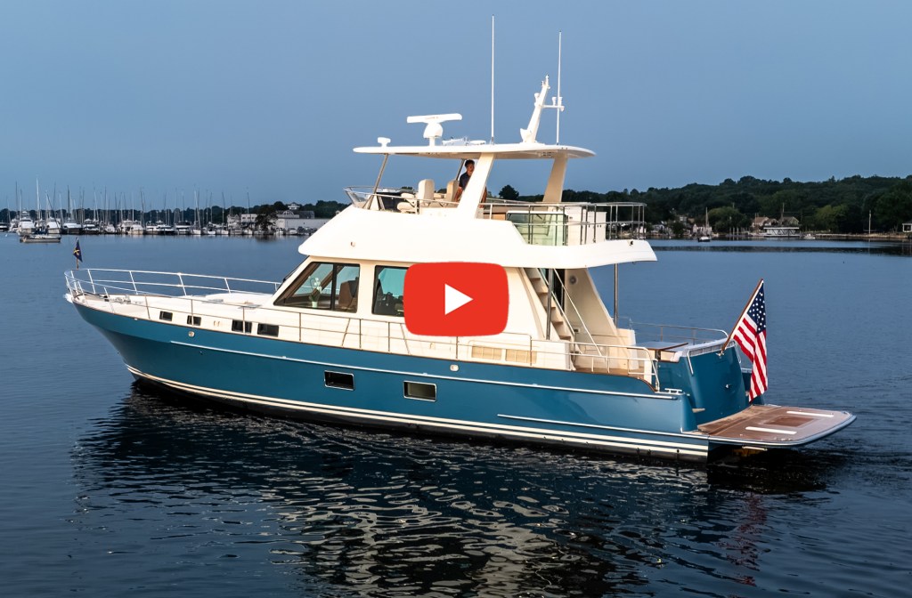 Feat Hunt 56 Side profile of a blue Hunt 56 motor yacht floating on calm water with a play video icon overlay.