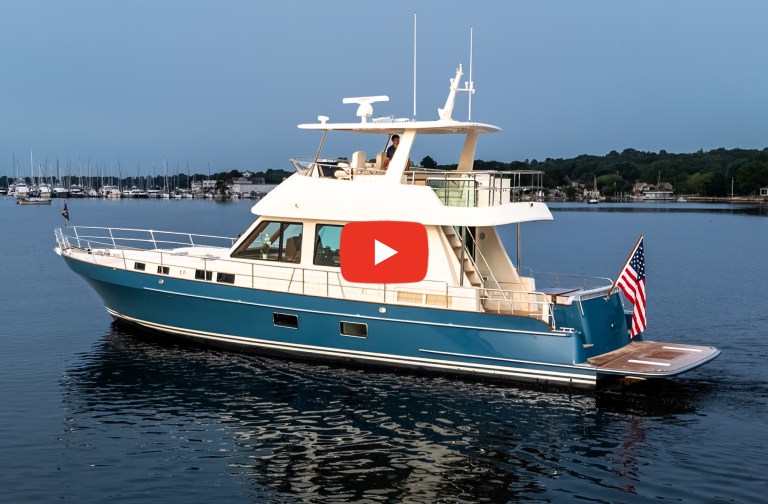 Feat Hunt 56 Side profile of a blue Hunt 56 motor yacht floating on calm water with a play video icon overlay.